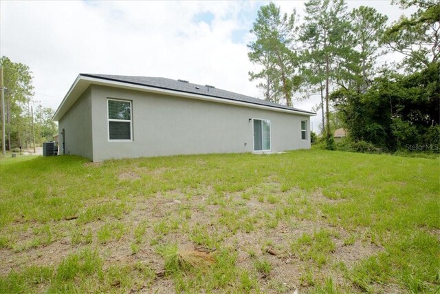 back of property with central air condition unit, a yard, and stucco siding