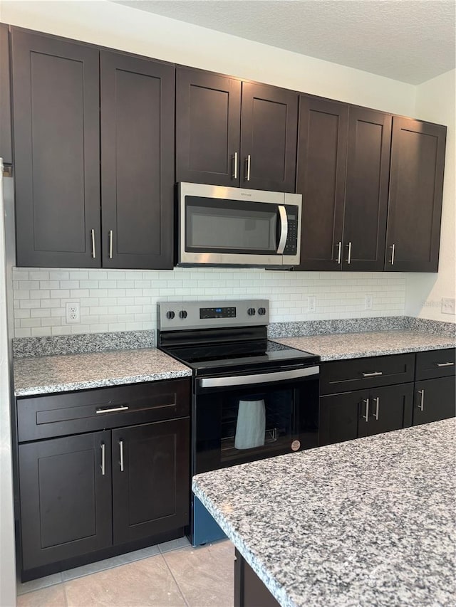 kitchen featuring tasteful backsplash, stainless steel microwave, electric range oven, light tile patterned flooring, and a textured ceiling