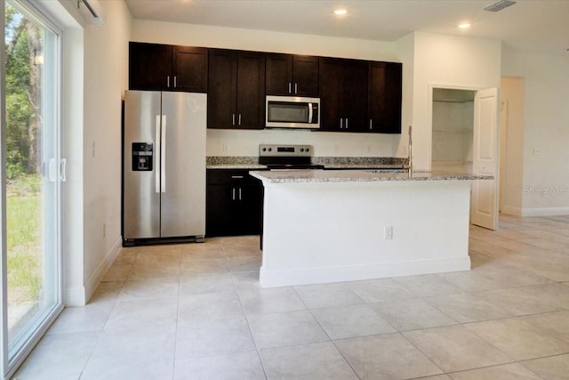 kitchen with stainless steel appliances, an island with sink, dark brown cabinetry, and a wealth of natural light