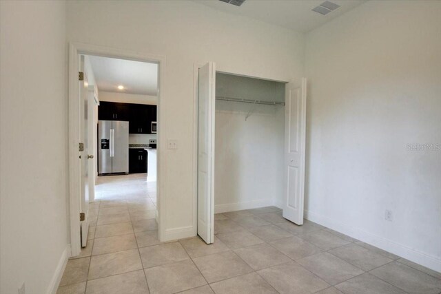 unfurnished bedroom featuring visible vents, a closet, light tile patterned flooring, stainless steel fridge with ice dispenser, and baseboards