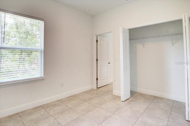 unfurnished bedroom featuring light tile patterned floors, baseboards, and a closet