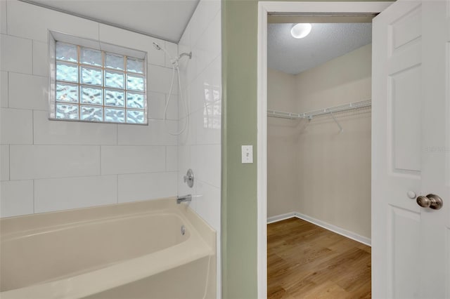 bathroom featuring wood-type flooring, tiled shower / bath combo, and a textured ceiling