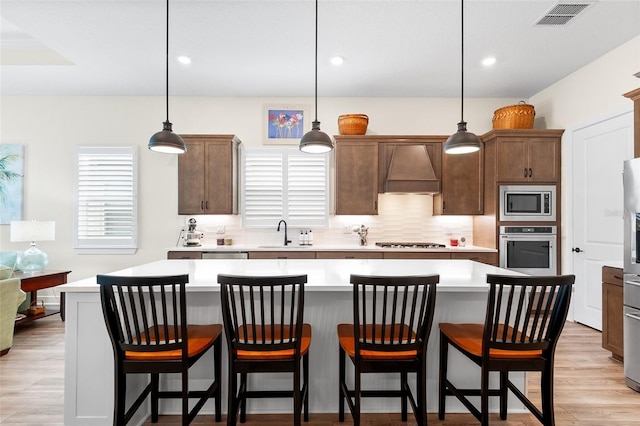 kitchen featuring a kitchen island, custom range hood, hanging light fixtures, and appliances with stainless steel finishes