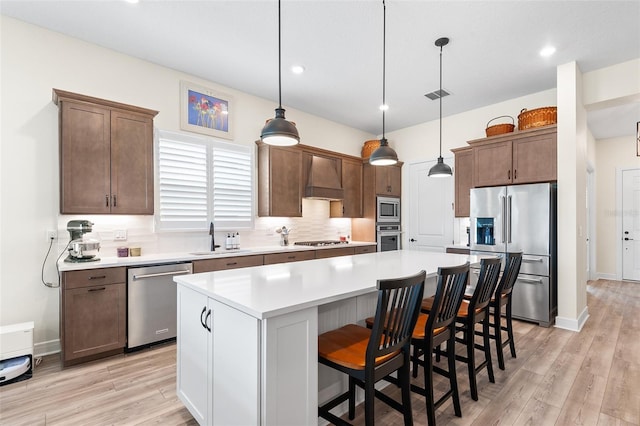 kitchen with appliances with stainless steel finishes, custom range hood, sink, a center island, and hanging light fixtures