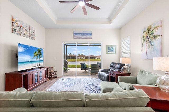 living room with wood-type flooring, a raised ceiling, ceiling fan, and ornamental molding