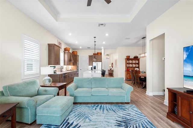 living room with light wood-type flooring, a raised ceiling, ceiling fan, and sink