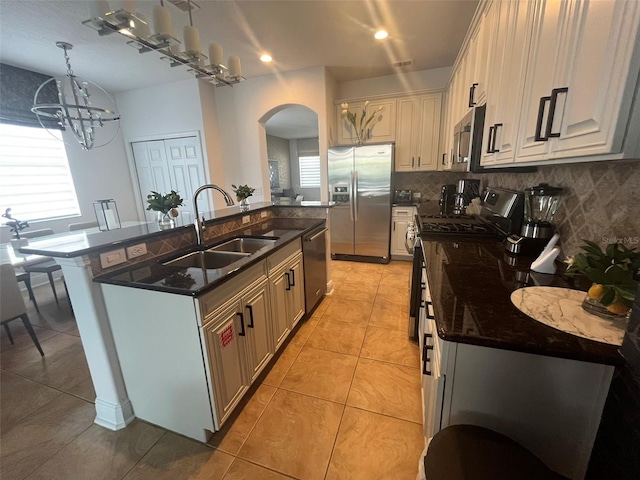 kitchen featuring a center island with sink, stainless steel appliances, backsplash, sink, and light tile flooring