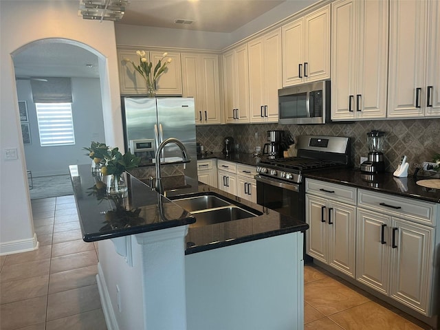 kitchen featuring a center island with sink, appliances with stainless steel finishes, backsplash, sink, and light tile floors