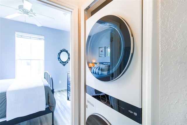 clothes washing area featuring ceiling fan, stacked washer / drying machine, and hardwood / wood-style flooring