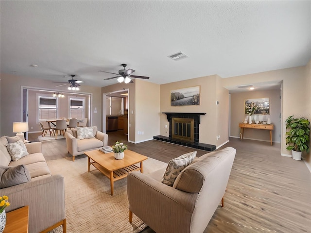 living room featuring ceiling fan, light hardwood / wood-style flooring, a tile fireplace, and a textured ceiling