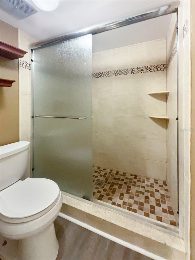 bathroom with toilet, a shower with door, and wood-type flooring