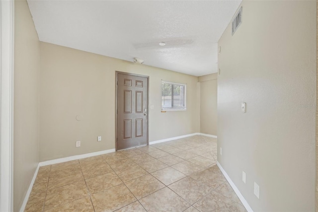 empty room with a textured ceiling and light tile patterned floors