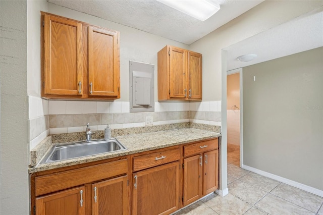 kitchen with sink, a textured ceiling, light tile patterned floors, and light stone counters