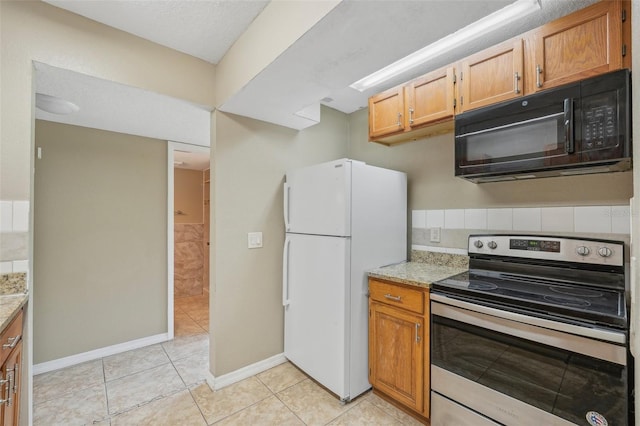 kitchen featuring light stone counters, white refrigerator, stainless steel electric range oven, and light tile patterned flooring