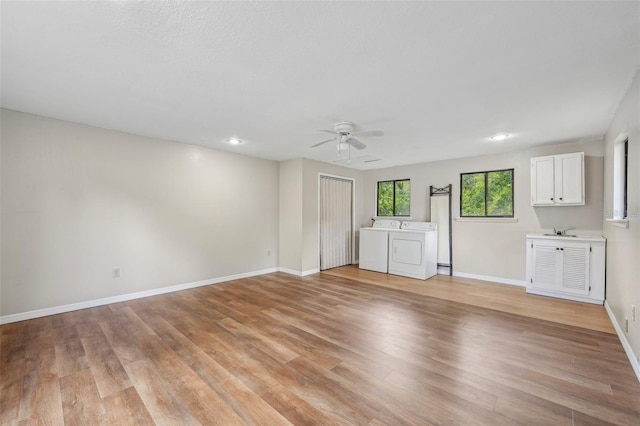 unfurnished living room with sink, light hardwood / wood-style floors, washer and clothes dryer, and ceiling fan