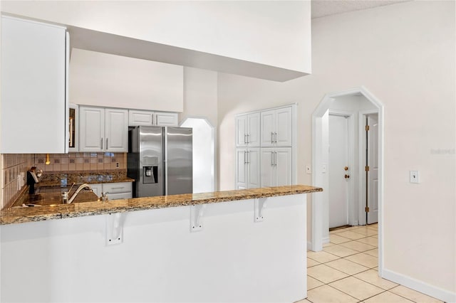 kitchen with kitchen peninsula, stainless steel fridge, white cabinets, and a breakfast bar area