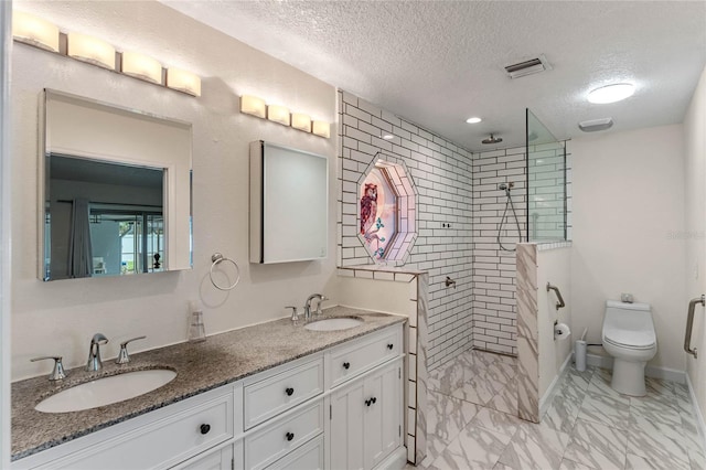 bathroom with vanity, a tile shower, a textured ceiling, and toilet