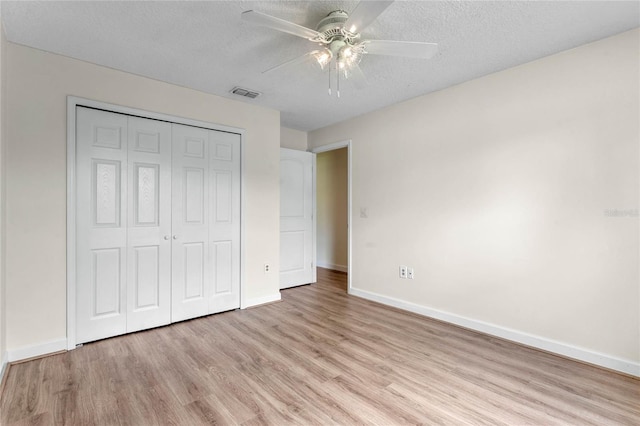 unfurnished bedroom featuring a textured ceiling, a closet, light hardwood / wood-style flooring, and ceiling fan