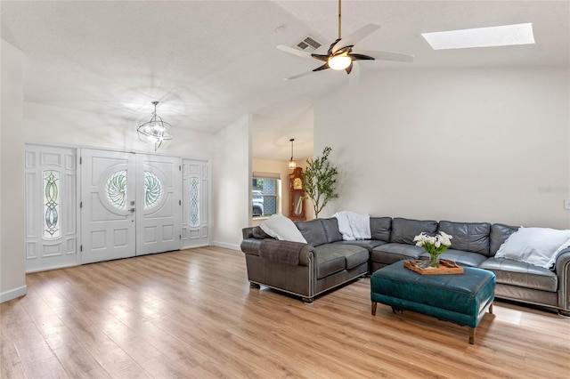 living room featuring ceiling fan with notable chandelier, light hardwood / wood-style floors, and lofted ceiling with skylight