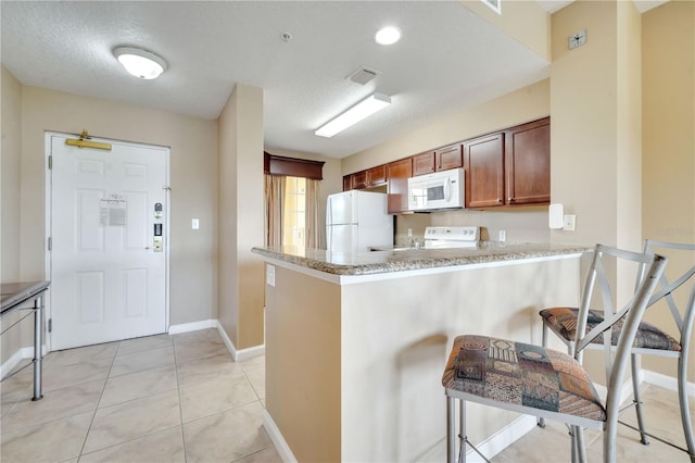 kitchen featuring light tile patterned flooring, a textured ceiling, white appliances, and kitchen peninsula