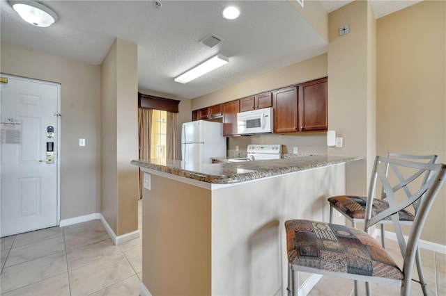 kitchen featuring kitchen peninsula, a textured ceiling, light tile patterned floors, and white appliances