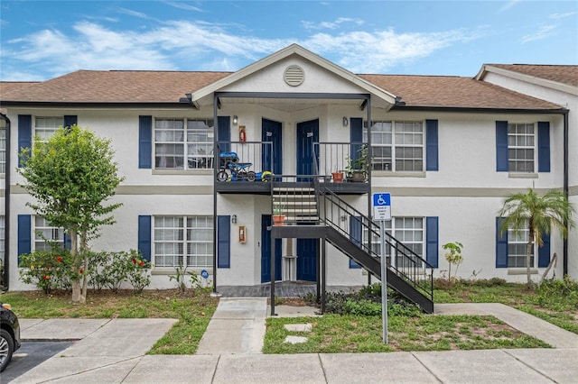 townhome / multi-family property featuring stucco siding, roof with shingles, covered porch, and stairs