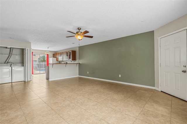 unfurnished living room featuring baseboards, ceiling fan, washing machine and dryer, light tile patterned floors, and a textured ceiling
