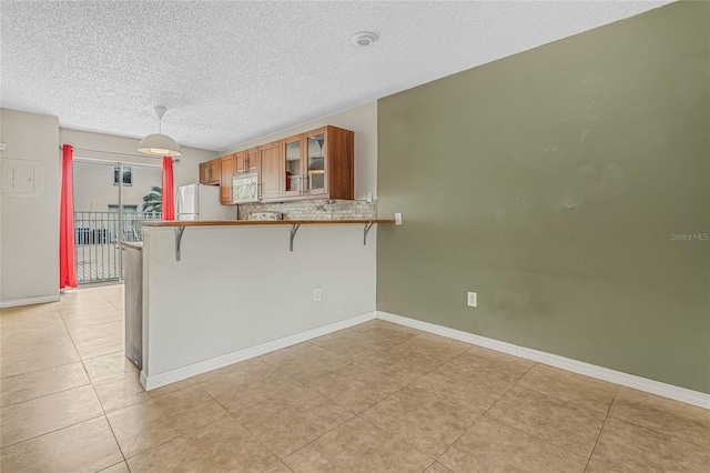 kitchen featuring glass insert cabinets, a breakfast bar area, a peninsula, brown cabinetry, and white appliances