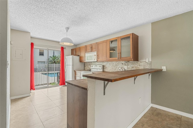 kitchen featuring kitchen peninsula, tasteful backsplash, a breakfast bar area, white appliances, and light tile floors