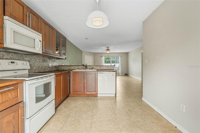 kitchen with glass insert cabinets, decorative backsplash, a peninsula, white appliances, and a sink