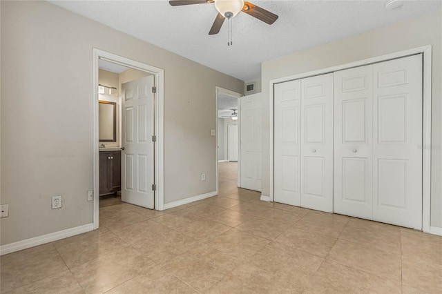 unfurnished bedroom featuring a closet, ceiling fan, light tile floors, ensuite bath, and a textured ceiling