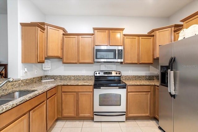 kitchen with stainless steel appliances, light tile patterned flooring, light stone counters, and sink