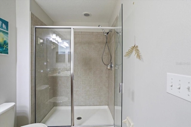 bathroom with a shower with door, a textured ceiling, and toilet