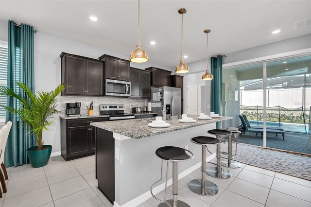 kitchen with stainless steel appliances, backsplash, hanging light fixtures, a center island, and light tile floors