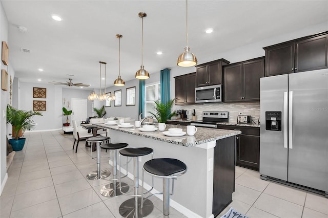 kitchen featuring hanging light fixtures, a center island with sink, stainless steel appliances, backsplash, and ceiling fan