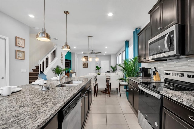 kitchen featuring light stone countertops, stainless steel appliances, backsplash, hanging light fixtures, and sink