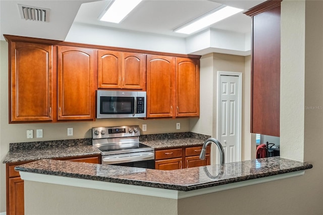 kitchen featuring stainless steel appliances, dark stone counters, visible vents, and a sink