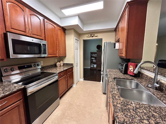 kitchen featuring a toaster, stainless steel appliances, a sink, dark stone counters, and baseboards