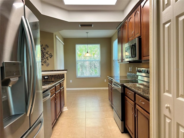 kitchen with light tile patterned flooring, stainless steel appliances, baseboards, hanging light fixtures, and dark stone counters