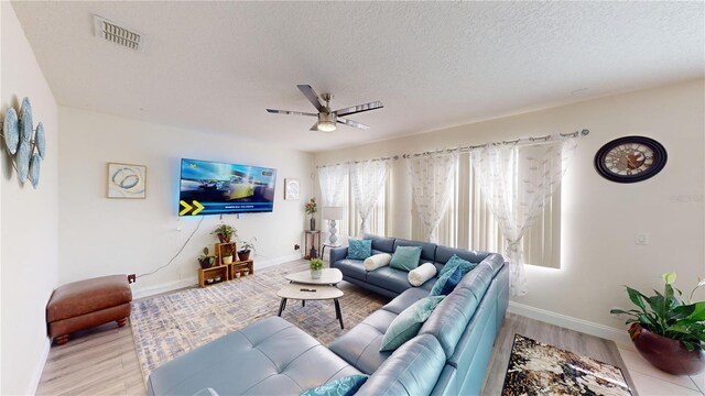 living room featuring ceiling fan, light hardwood / wood-style flooring, and a textured ceiling