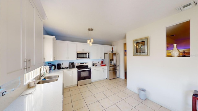 kitchen featuring stainless steel appliances, sink, light tile patterned floors, white cabinetry, and hanging light fixtures