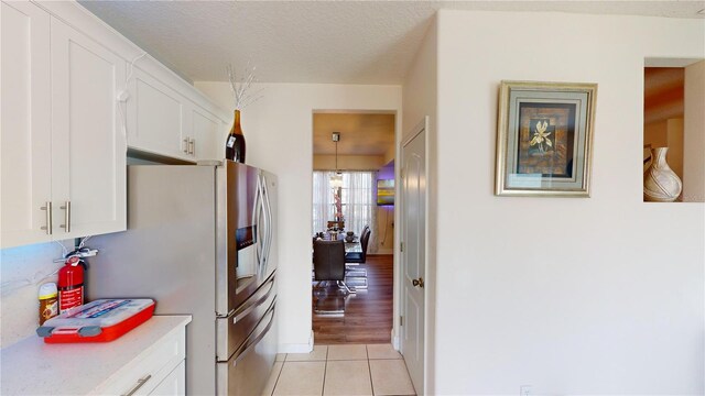 kitchen with white cabinetry, hanging light fixtures, stainless steel refrigerator with ice dispenser, a textured ceiling, and light wood-type flooring