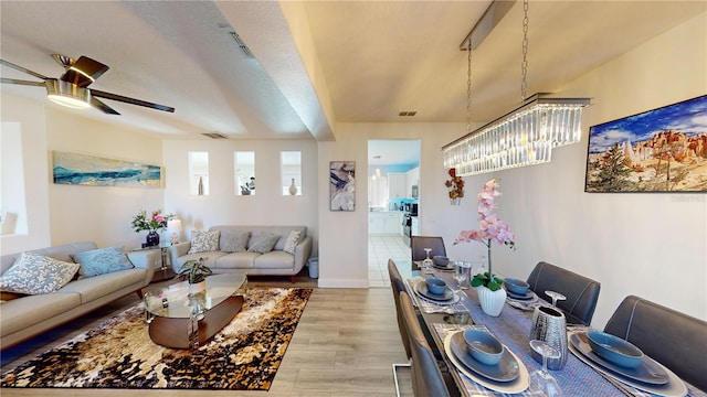 living room featuring ceiling fan with notable chandelier, a textured ceiling, and light wood-type flooring