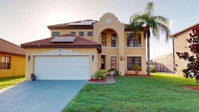 mediterranean / spanish-style house with concrete driveway, a front yard, roof mounted solar panels, stucco siding, and a garage