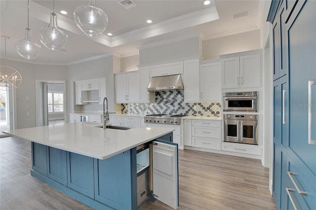 kitchen with sink, a large island with sink, white cabinets, hanging light fixtures, and range hood