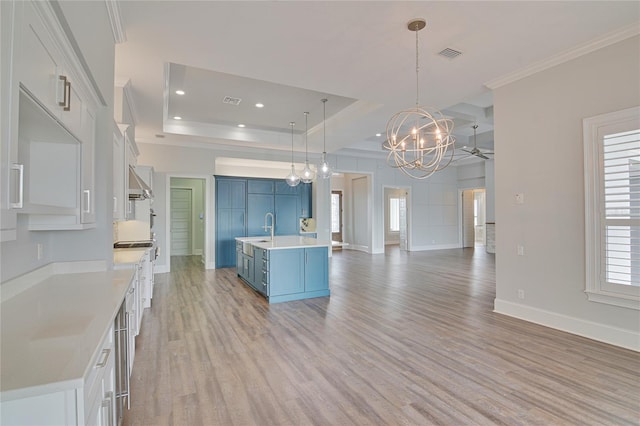 kitchen with blue cabinetry, a raised ceiling, white cabinetry, and an island with sink