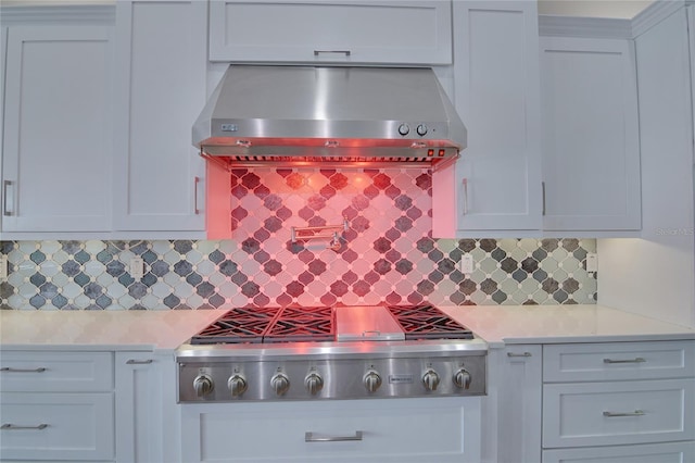 kitchen with wall chimney range hood, decorative backsplash, light stone countertops, white cabinetry, and stainless steel gas cooktop