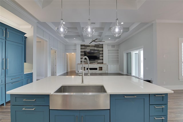 kitchen featuring built in shelves, sink, coffered ceiling, beamed ceiling, and a center island with sink