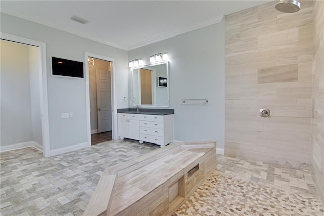 bathroom with a tile shower, vanity, and ornamental molding