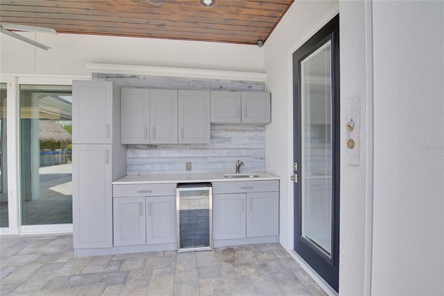 kitchen with sink, beverage cooler, wooden ceiling, gray cabinets, and decorative backsplash